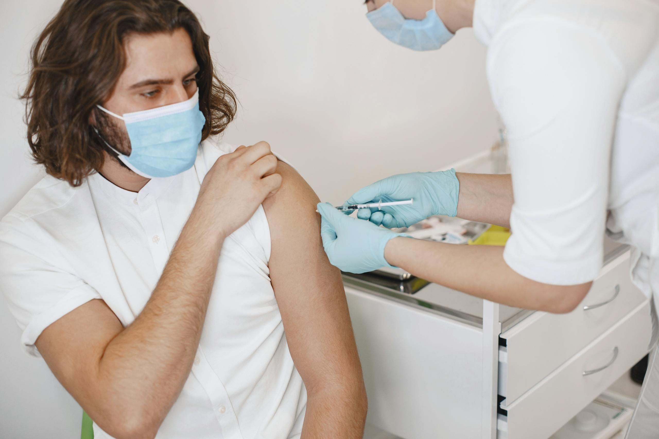 A healthcare worker administers a vaccine to a patient in a clinic. Safety measures are observed with masks and gloves.